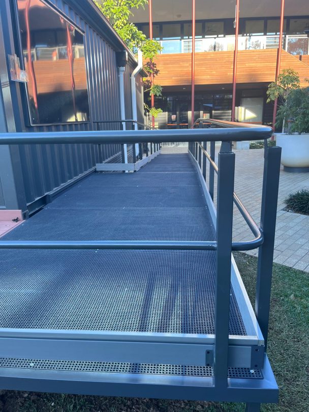 Close-up of the access ramp's grated surface and grey handrails running alongside the corrugated container wall