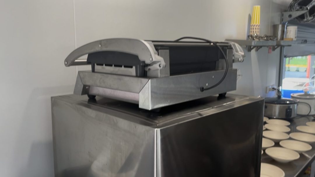 Commercial contact grill on a stainless steel cabinet inside the container kitchen