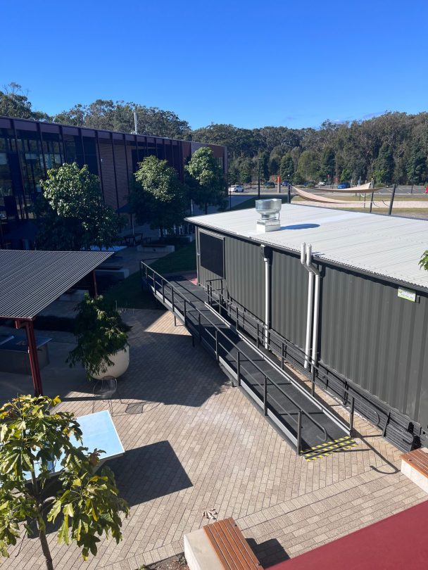 View from above of the container roof with a rooftop exhaust flue, and a long access ramp with handrails running along its side