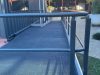 Close-up of the access ramp's grated surface and grey handrails running alongside the corrugated container wall