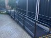 Long access ramp with handrails and a yellow and black warning strip at its base, running beside the dark container wall with downpipes and a rooftop flue