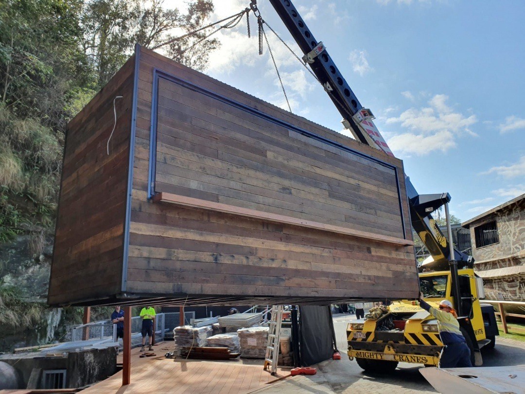 Finished timber-clad container module being craned into place on site