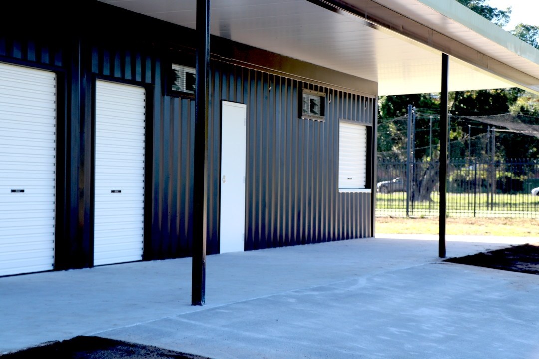 Dark shipping container multi-use amenities block with white flyover roof and concrete apron — Container Build Group