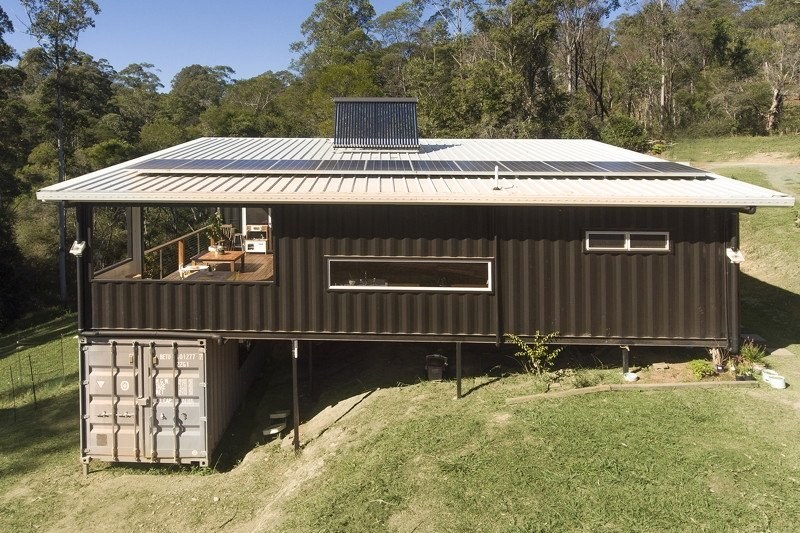 Container home raised on steel posts over a sloping block, with a 20ft container used for storage underneath