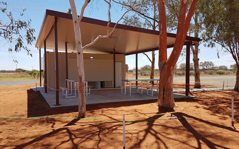 CBG container ablution block installed under a steel shade roof with picnic tables on a red-dirt outback site