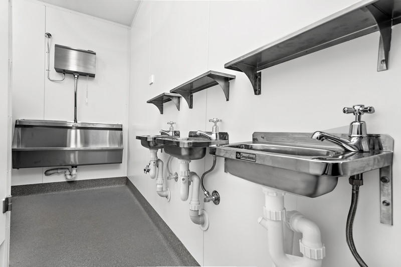 Inside a CBG container ablution block with stainless steel basins, shelves and a trough urinal
