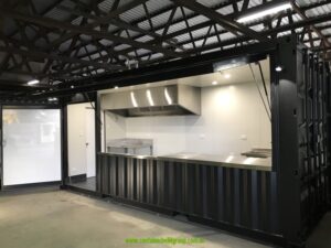 Side view of a black 20ft commercial kitchen container with the servery open and a white lined, insulated interior