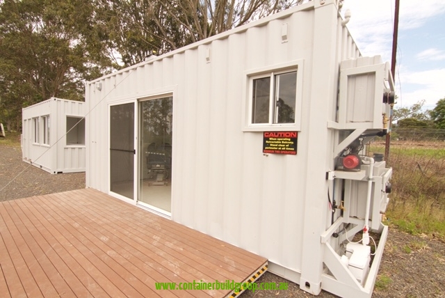 20ft off-grid mobile clinic built by Container Build Group, with a sliding glass door, timber deck and service enclosures on the end wall.
