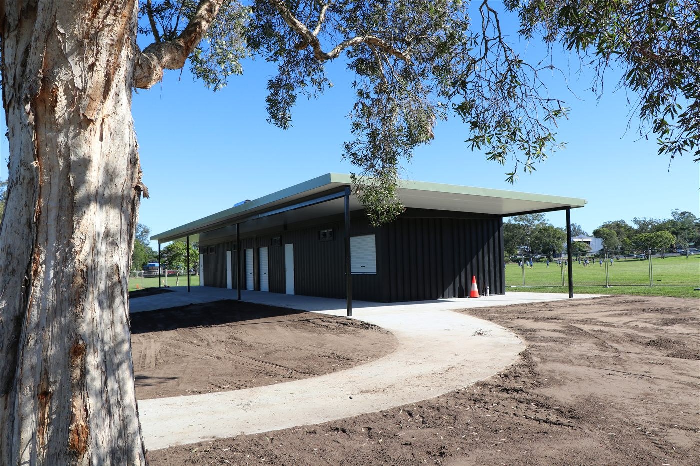 Mortimer Oval container change rooms and canteen stores in Lismore seen past a gum tree, with a new concrete path leading to the building