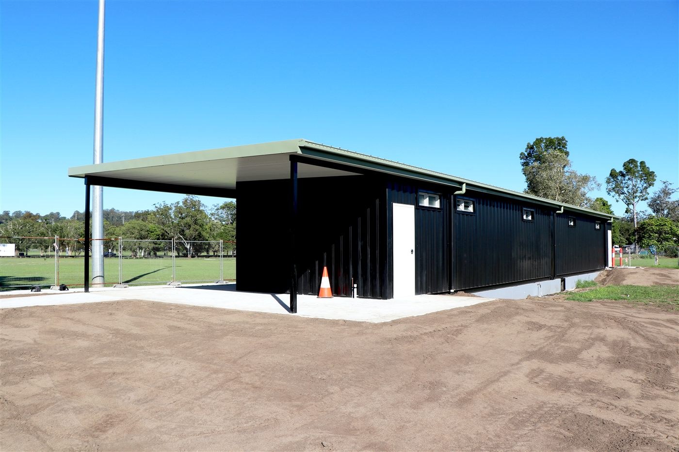 Side view of the black shipping container change rooms at Mortimer Oval, Lismore, under a long skillion roof beside the sports field